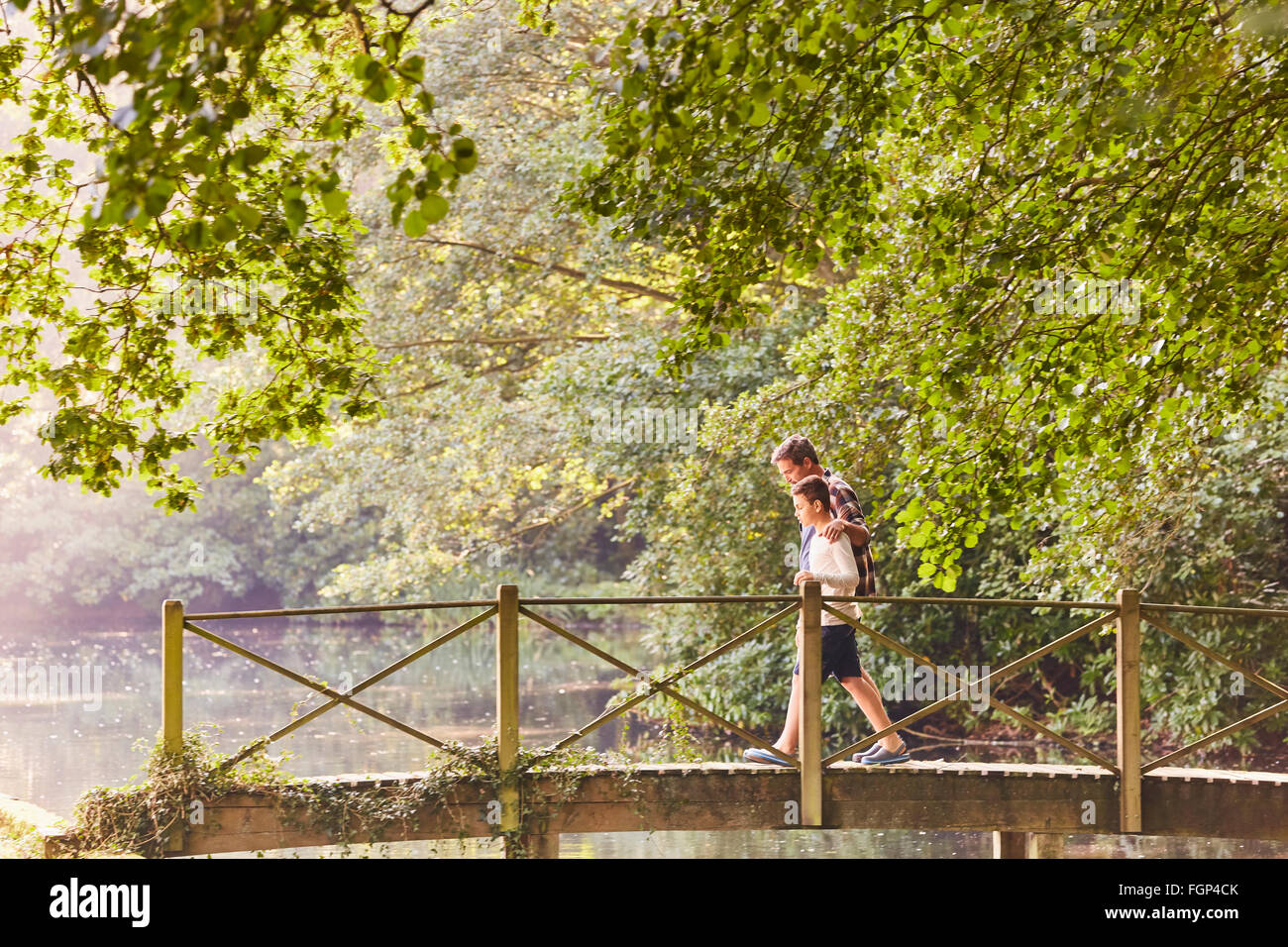 Father and son crossing footbridge in park with trees Stock Photo