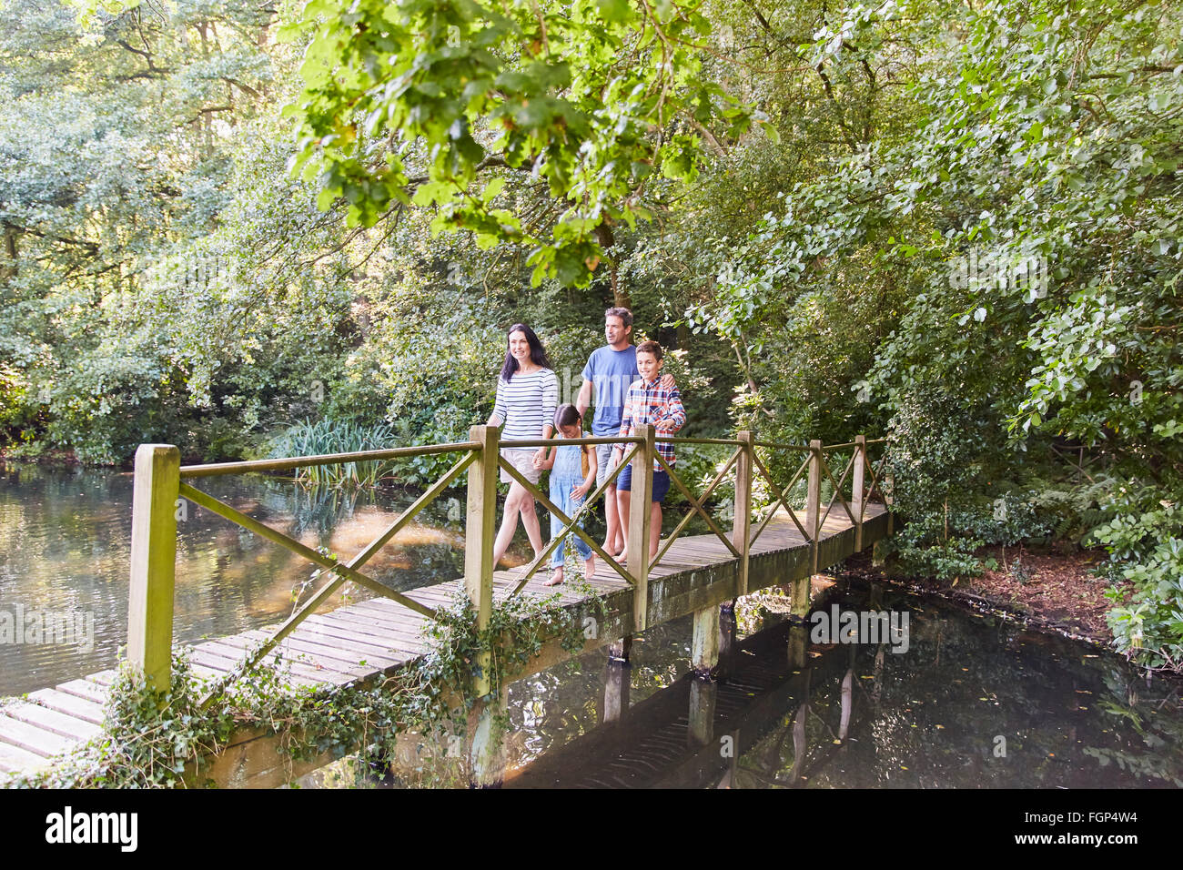 Family crossing footbridge in park with trees Stock Photo