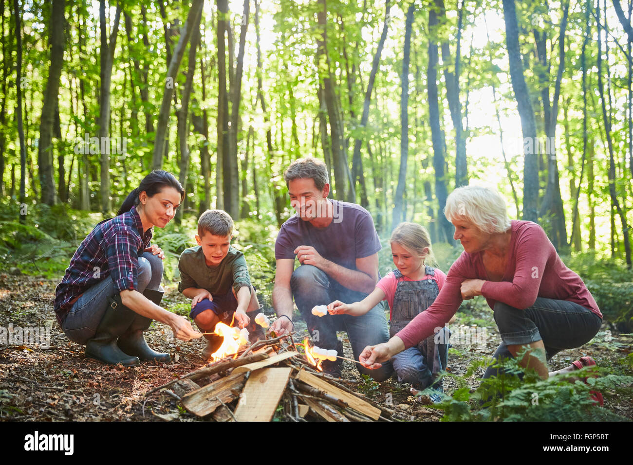 Multi-generation family roasting marshmallows at campfire in forest Stock Photo