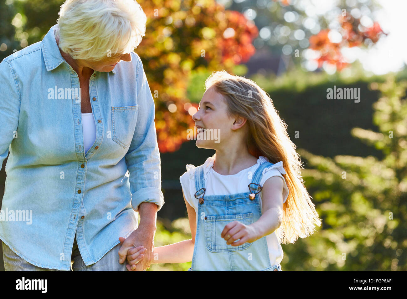 Grandmother and granddaughter holding hands and walking in sunny garden Stock Photo