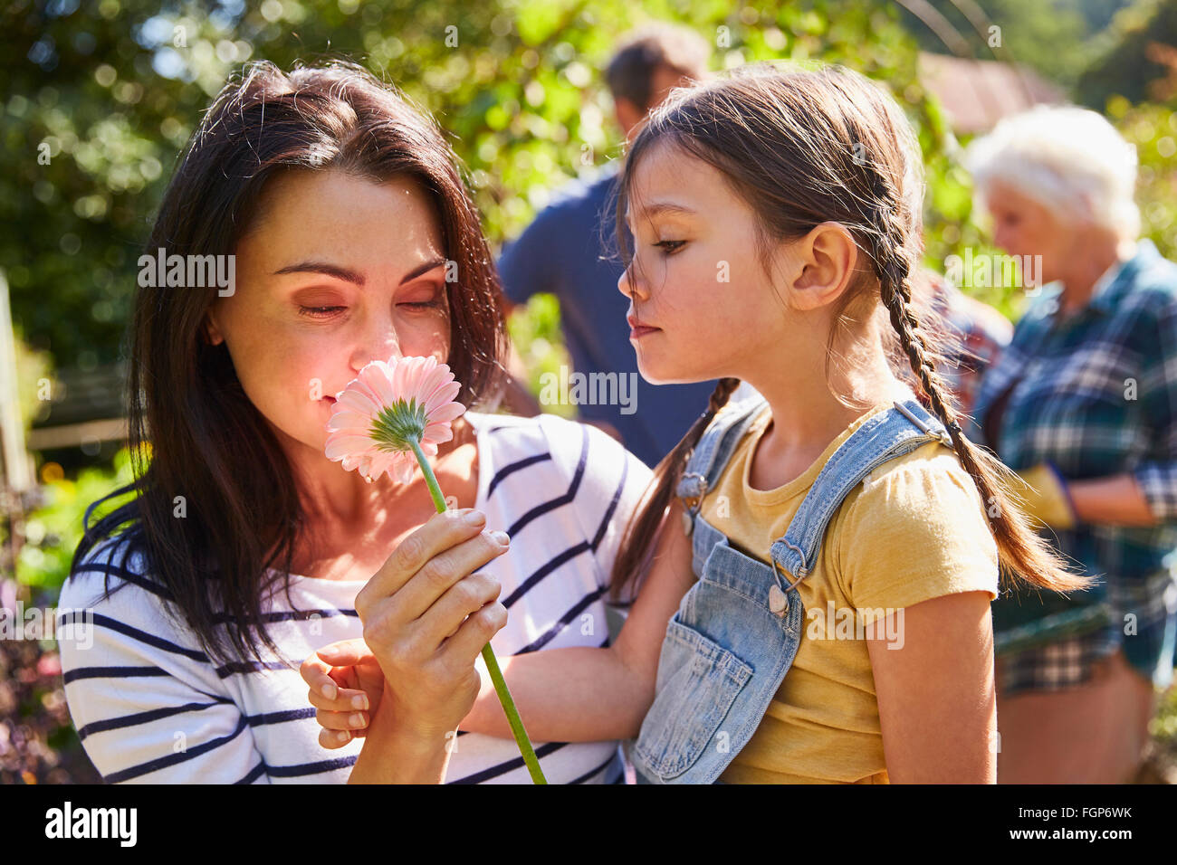 Mother and daughter smelling fresh pink flower in sunny garden Stock Photo