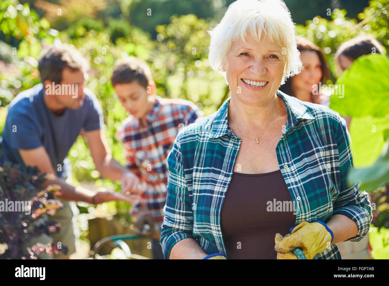 Portrait smiling senior woman in sunny garden with family Stock Photo