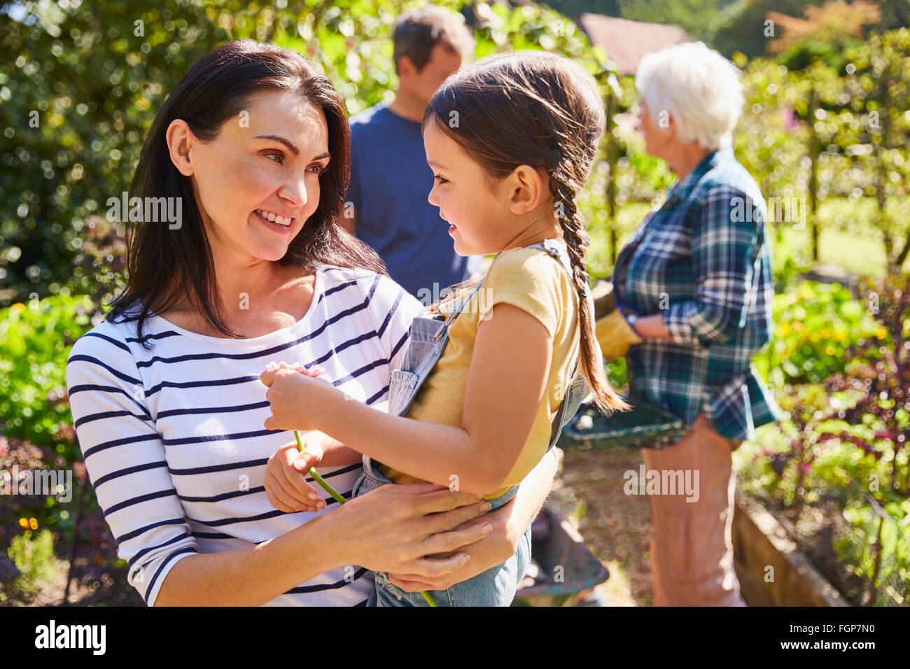 Affectionate mother holding daughter in sunny garden Stock Photo