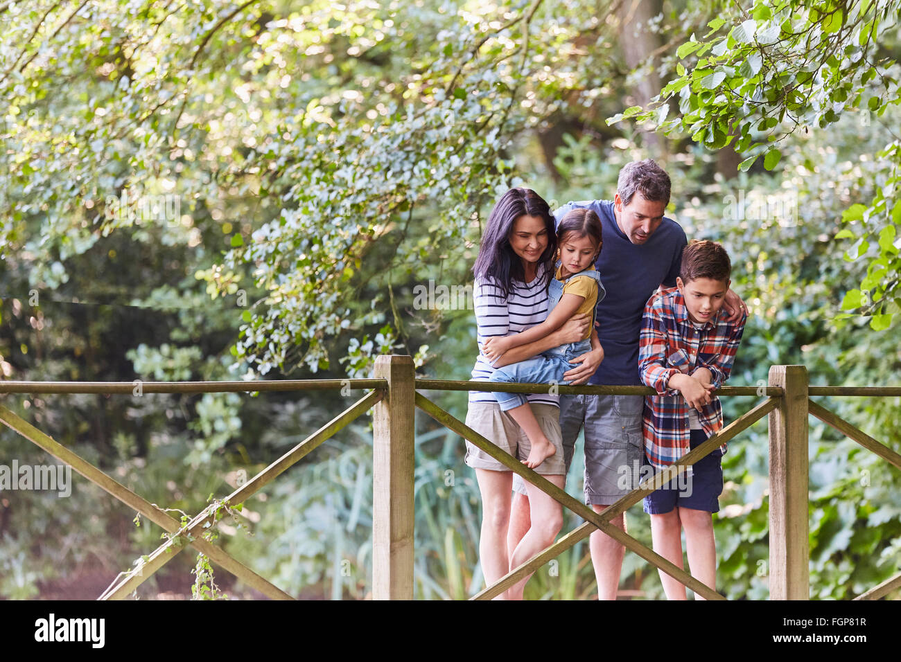 Family standing on footbridge in park with trees Stock Photo