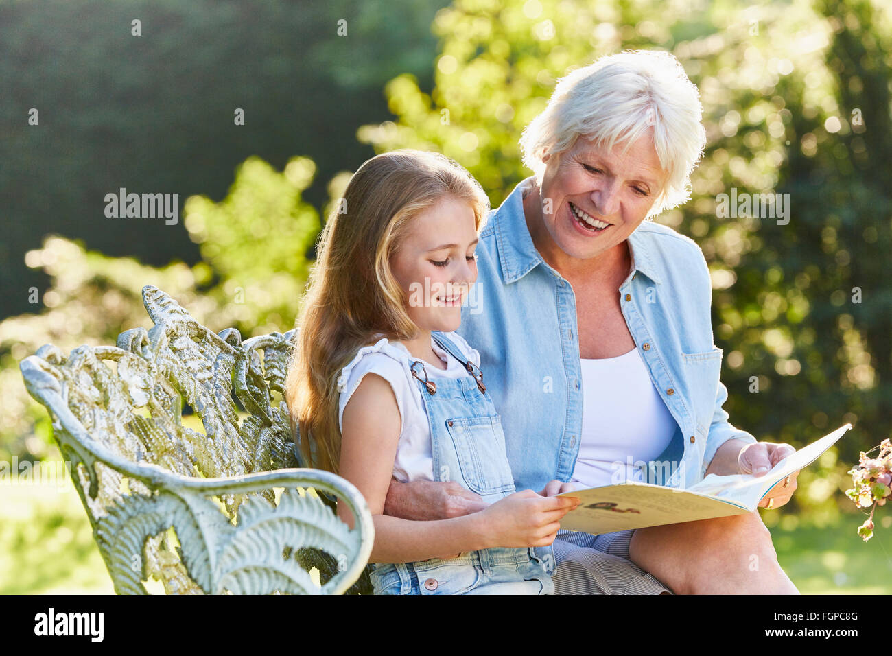 Grandmother reading with granddaughter on garden bench Stock Photo