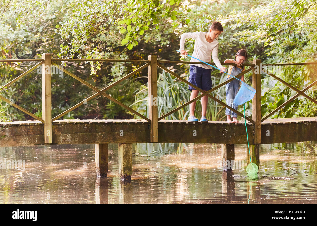 Brother and sister fishing with nets at footbridge over pond Stock Photo