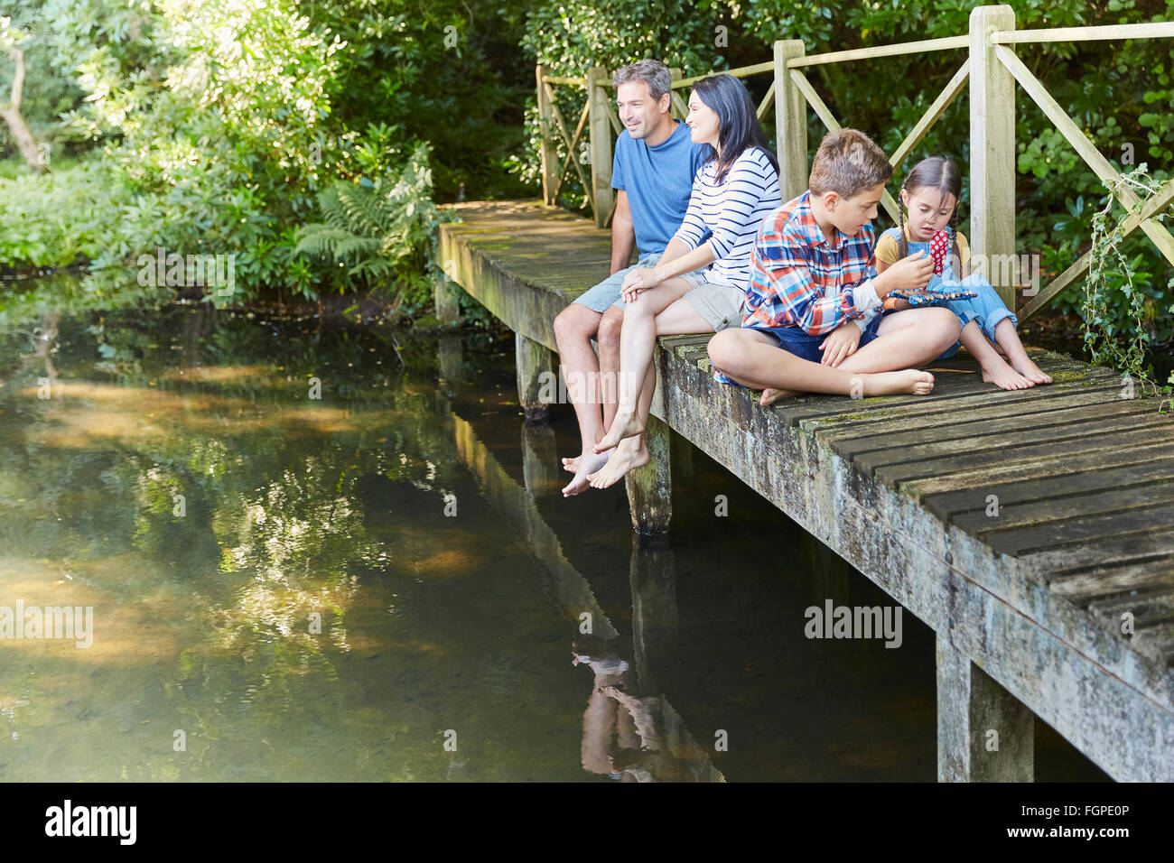 Family relaxing on footbridge over pond Stock Photo