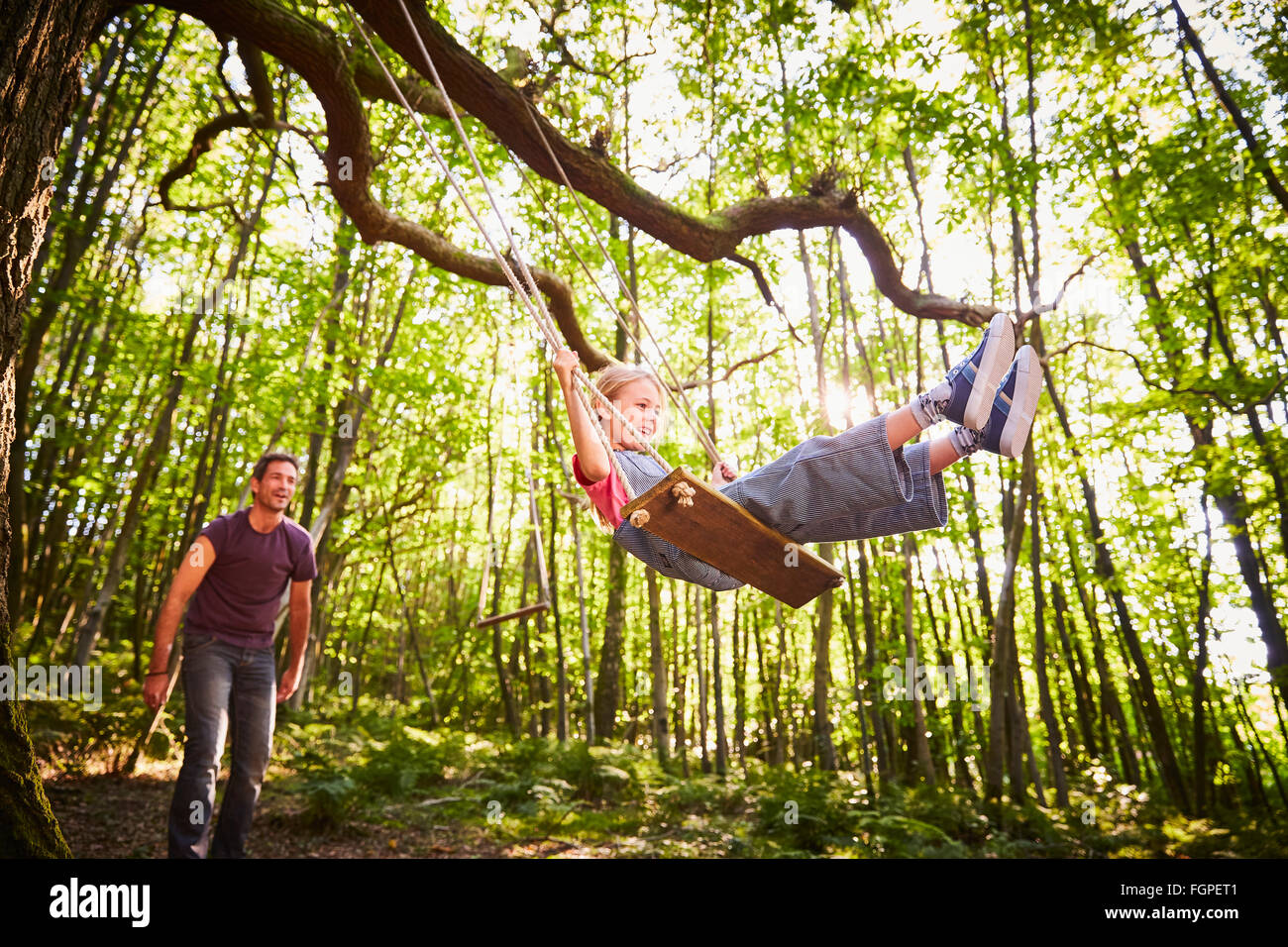 Father pushing daughter on rope swing in forest Stock Photo