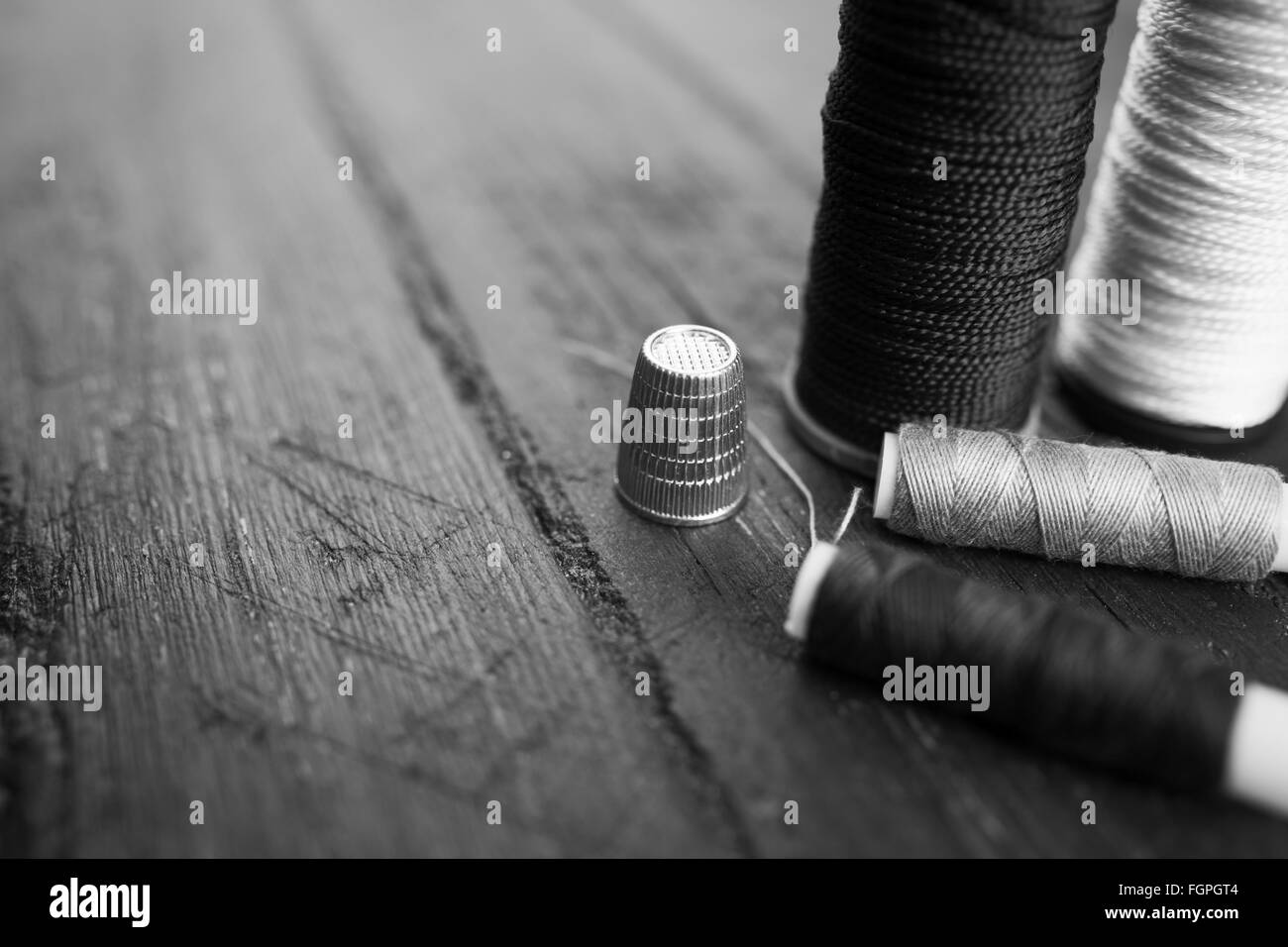 Sewing accessories: bobbins of thread, needle, thimble on wooden table. Black and white photo. Tailoring and sewing concept. Stock Photo