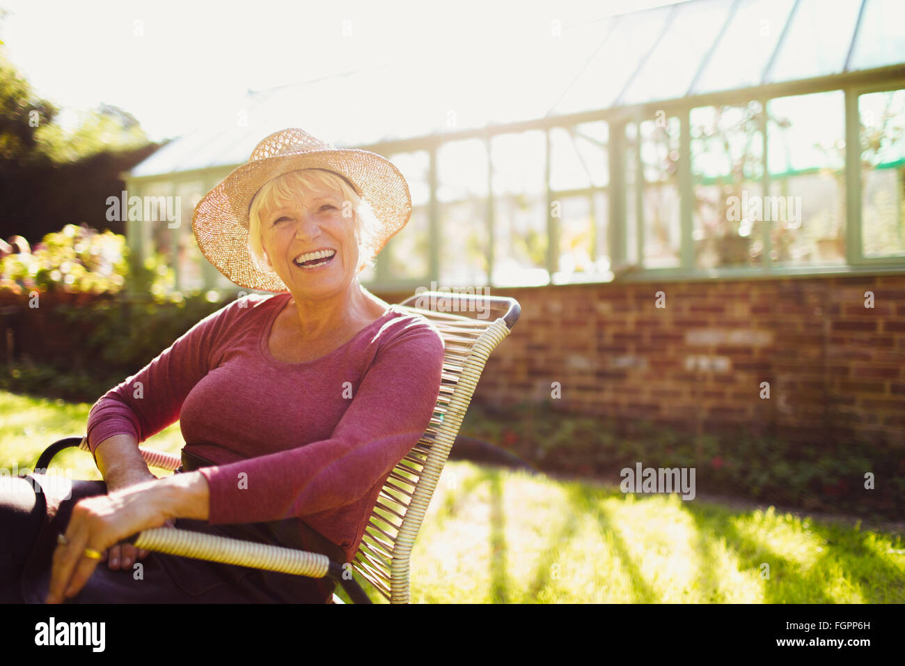 Portrait enthusiastic senior woman sitting outside sunny greenhouse Stock Photo