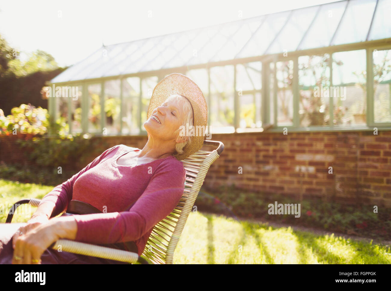 Carefree senior woman relaxing outside sunny greenhouse Stock Photo