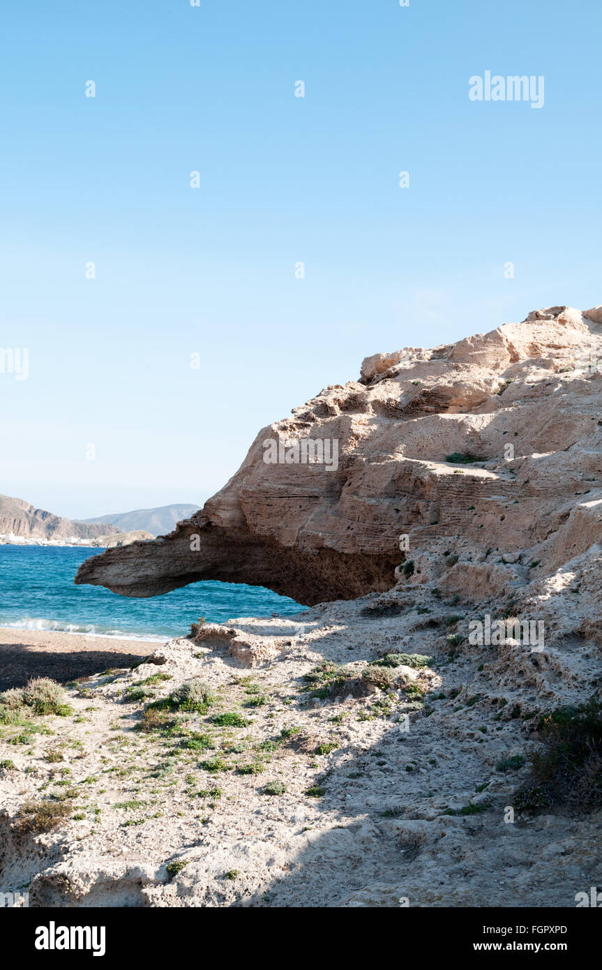 Volcanic rock formations at Los Escullos, Cabo de Gata National Park with the small fishing village of Isleta del Moro in rear Stock Photo