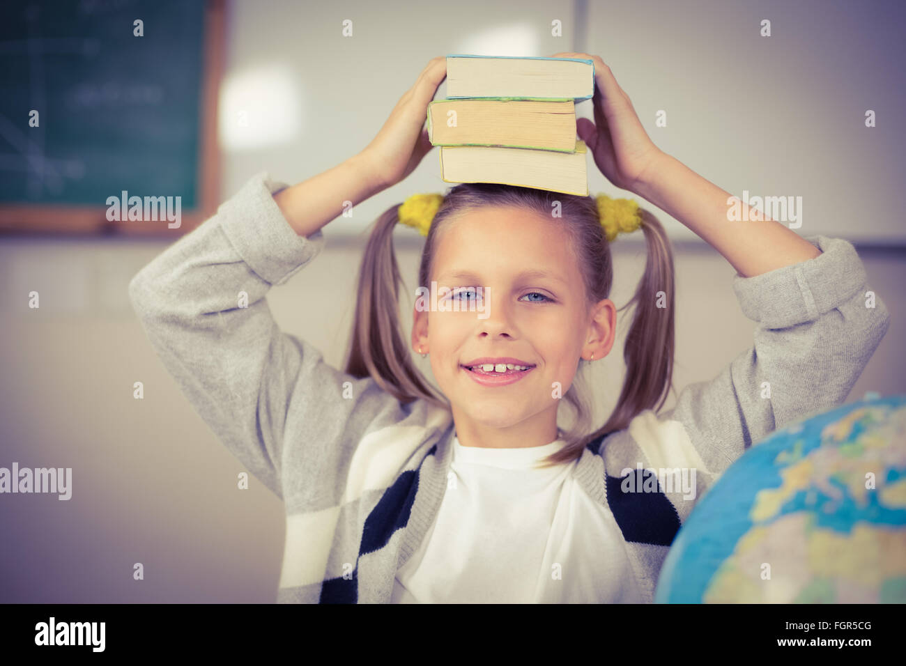 Cute pupil balancing books on head in a classroom Stock Photo - Alamy