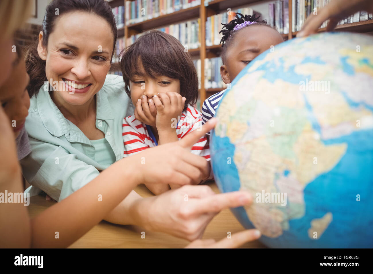Pupils and teacher looking at globe in library Stock Photo - Alamy