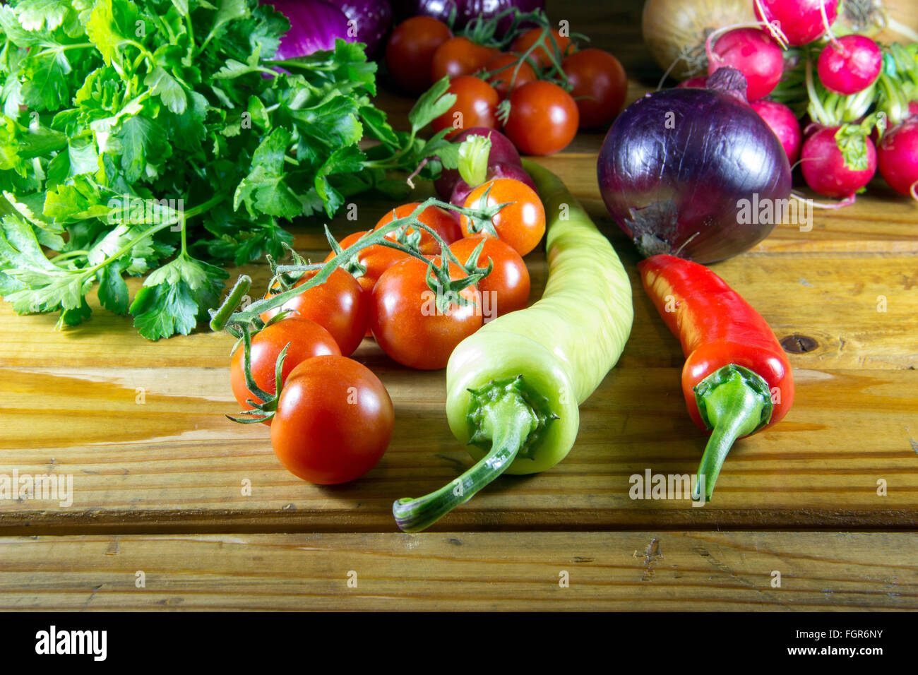 Peppers, tomato, radish, parsley and onions scattered on an old wooden table Stock Photo