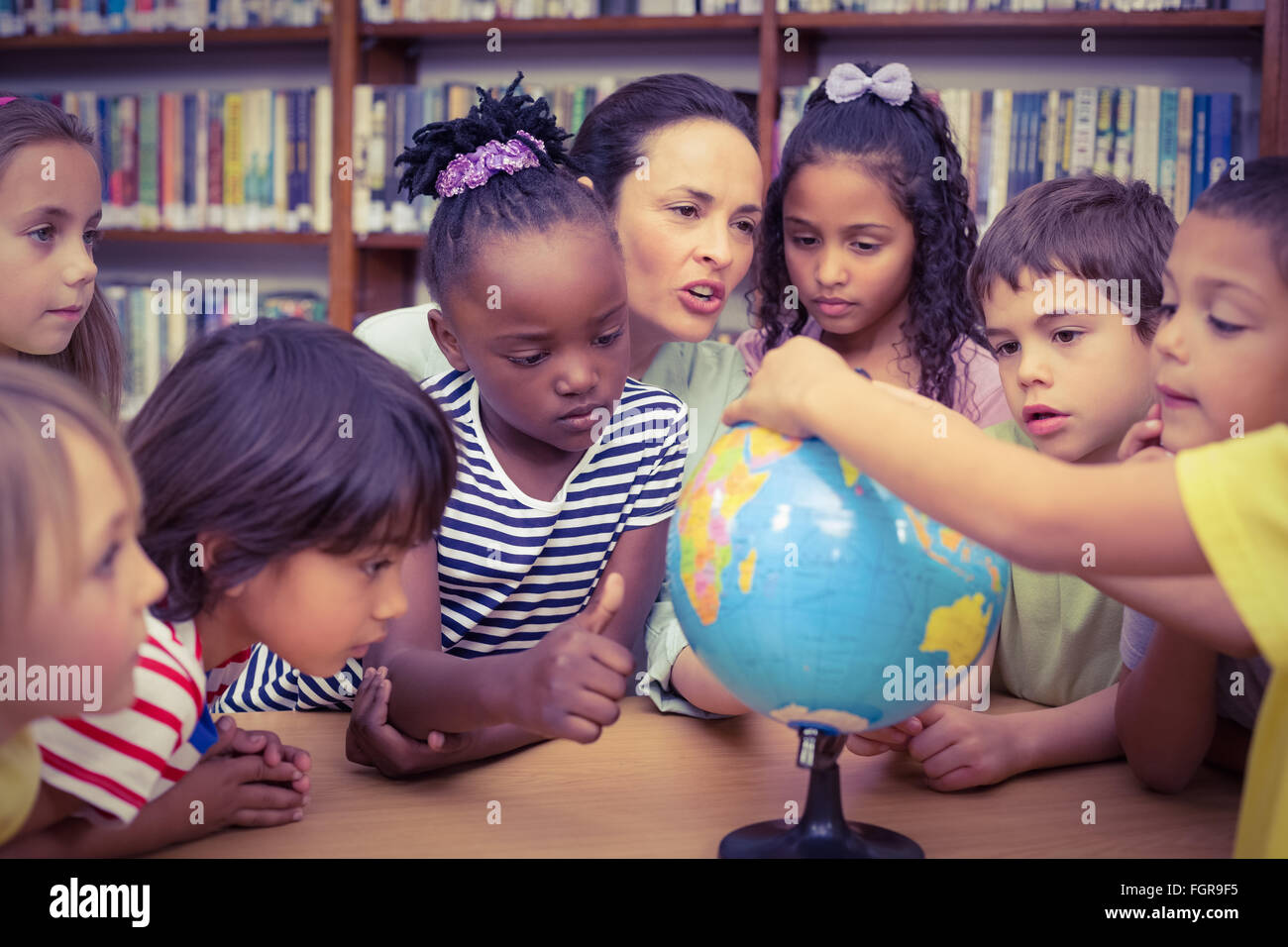 Pupils and teacher looking at globe in library Stock Photo - Alamy