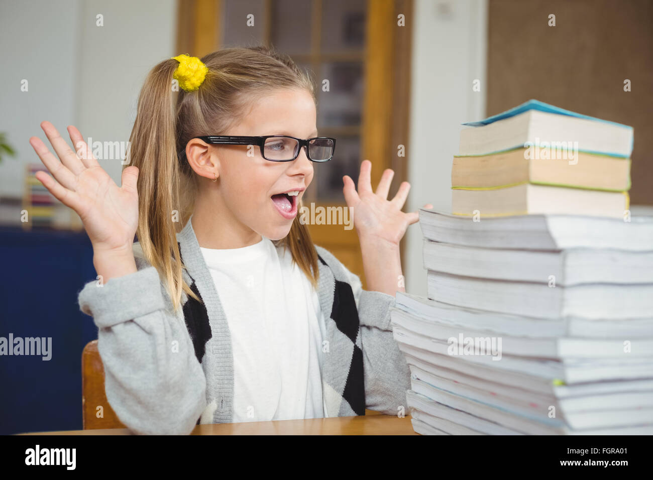 Pupil looking surprised at stack of books on her desk Stock Photo - Alamy