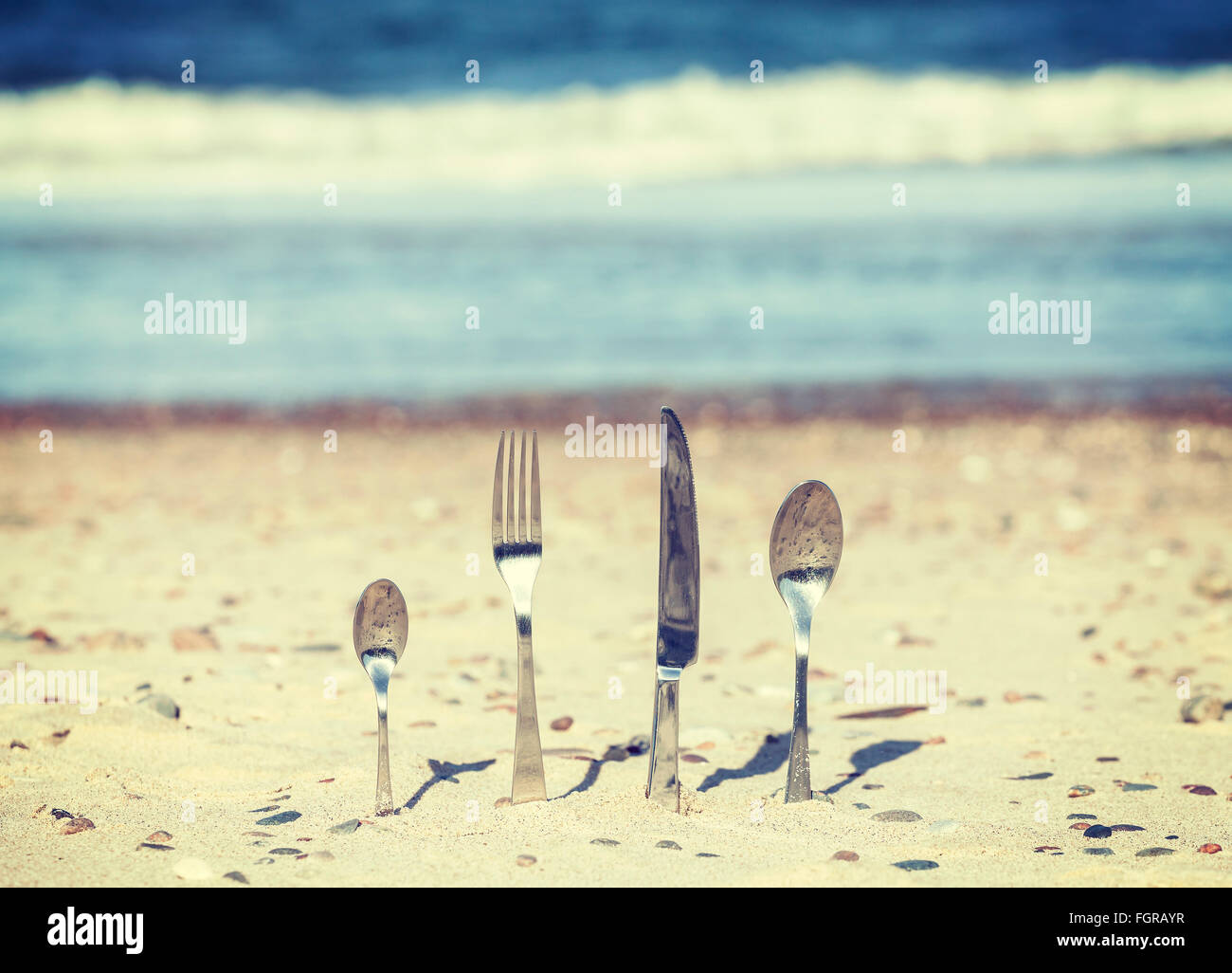 Retro toned cutlery stuck in sand on the beach, shallow depth of field. Stock Photo