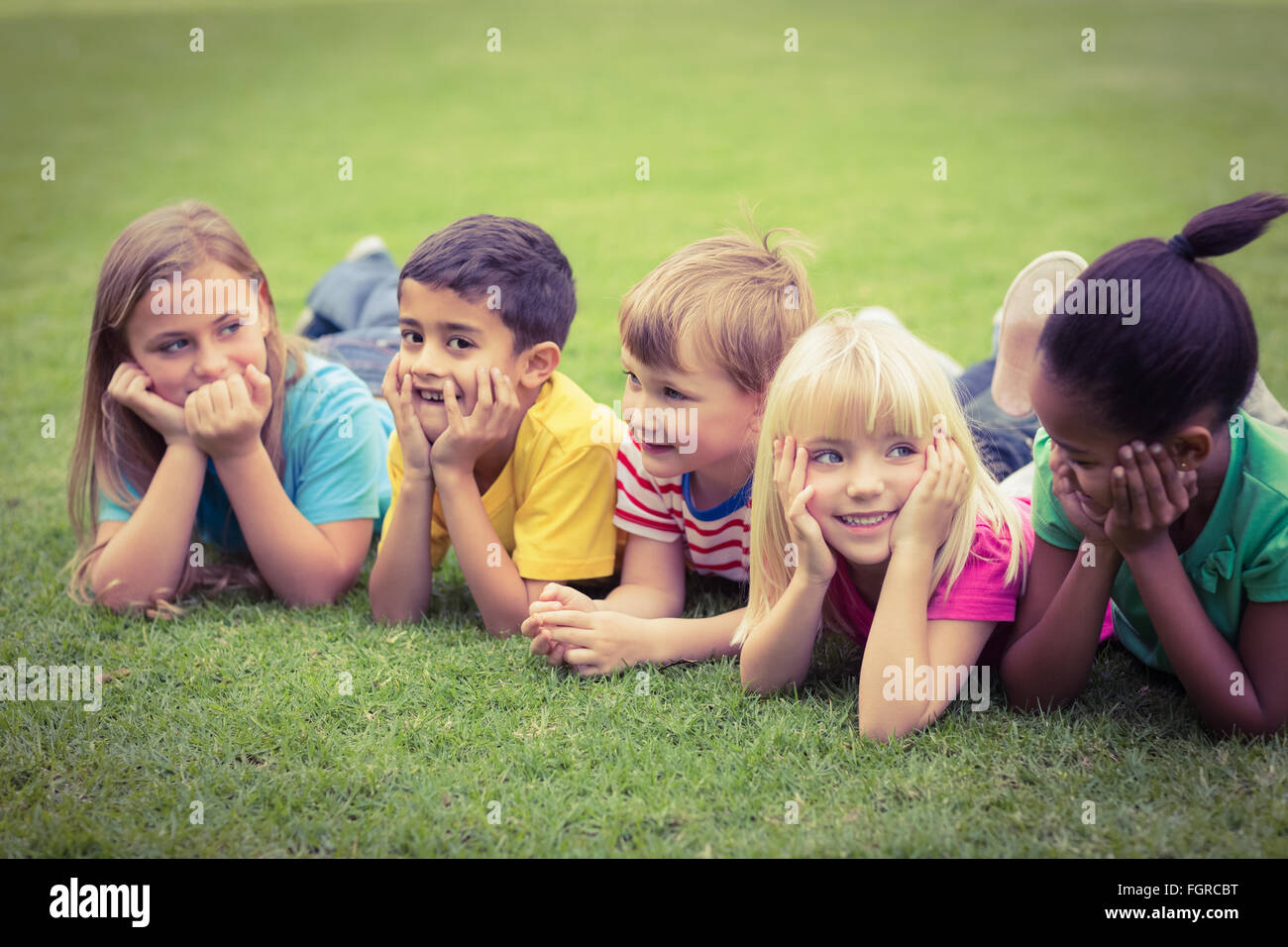 Smiling classmates lying in a row in grass Stock Photo