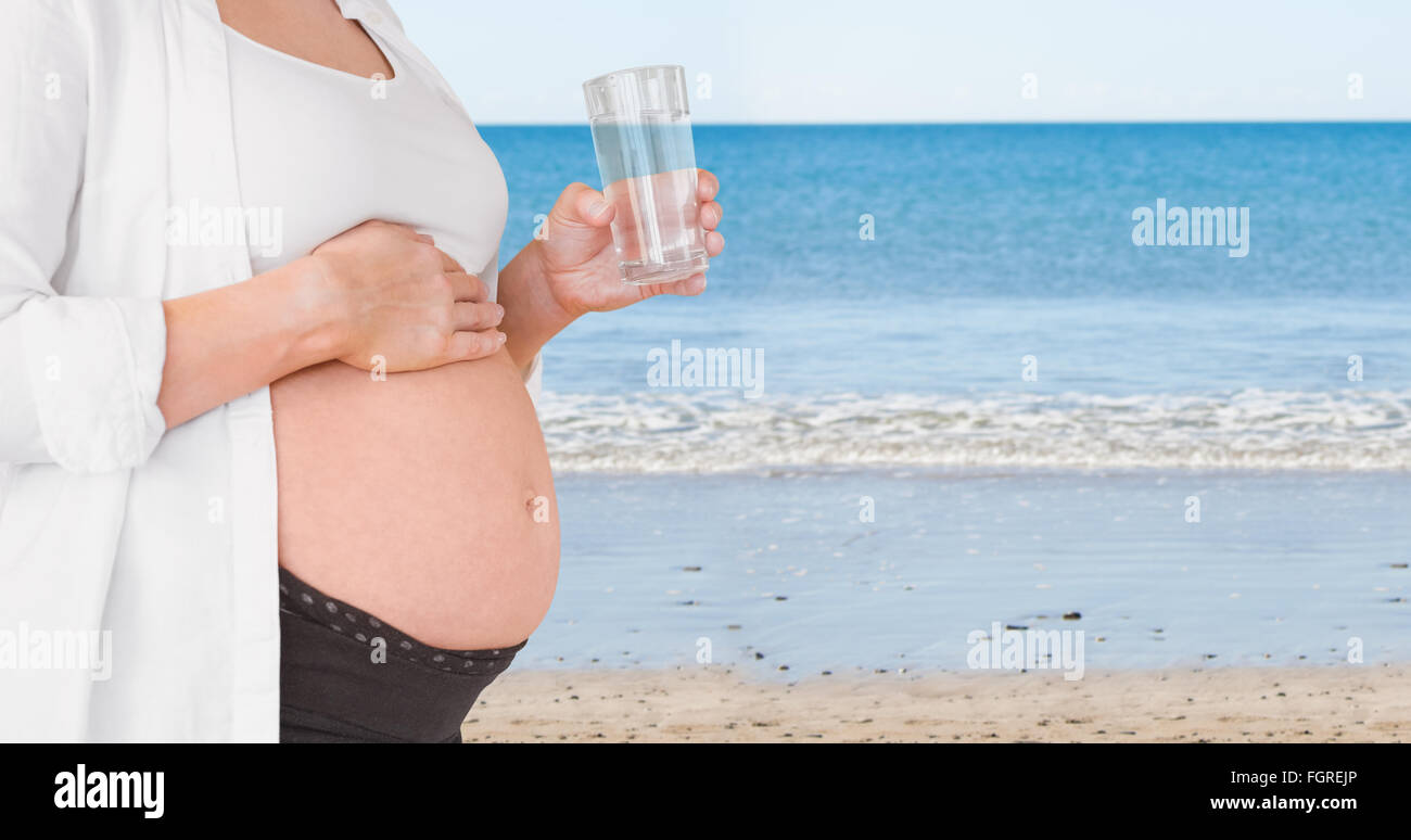 Composite image of midsection of expecting woman holding glass of water Stock Photo