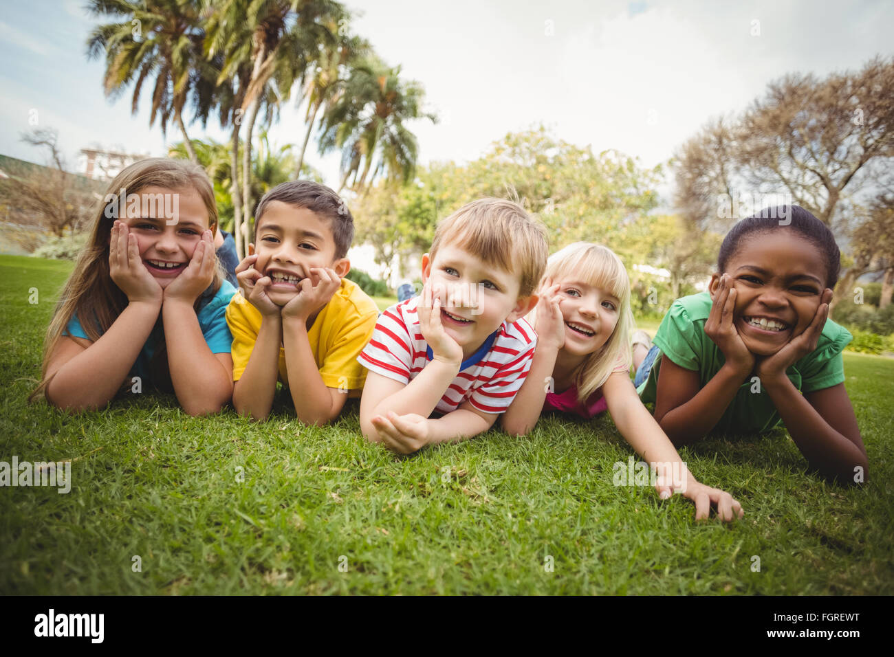 Smiling classmates lying in a row in grass Stock Photo