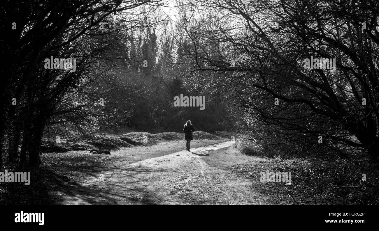 Black and white atmospheric shot of young lady walking in a park under arch of branches Milton country park Stock Photo