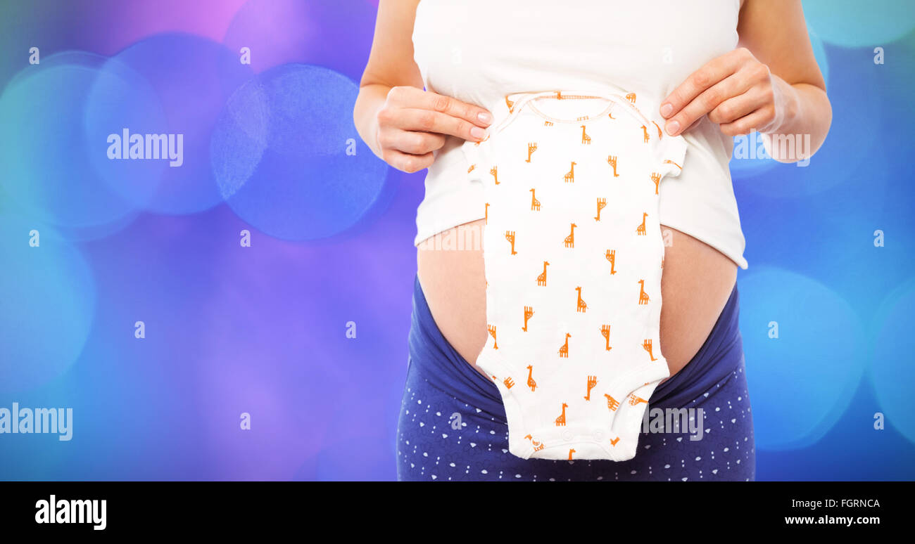 Composite image of pregnant woman holding baby clothes Stock Photo