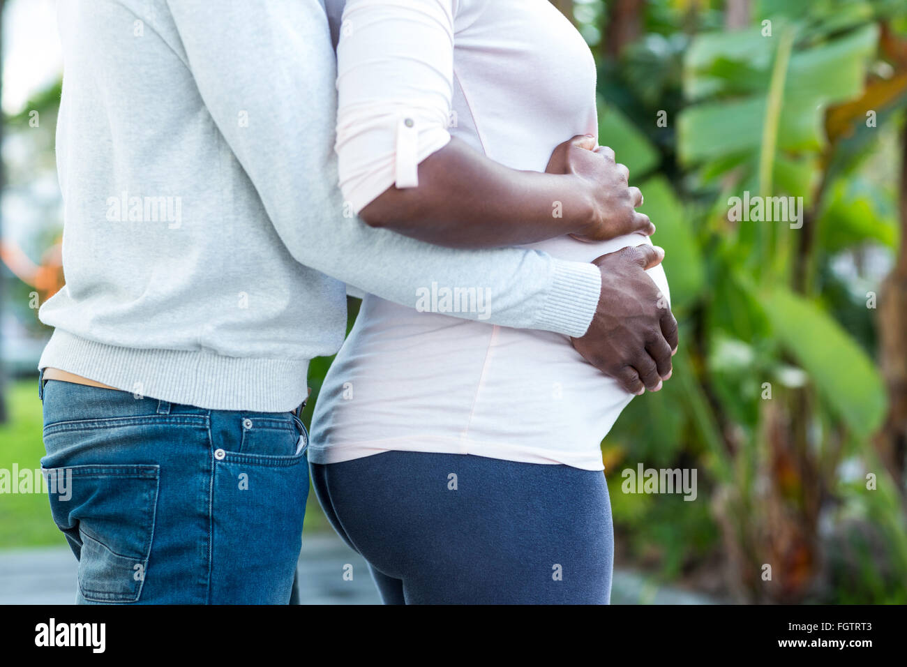 Husband embracing while wife touching her belly Stock Photo