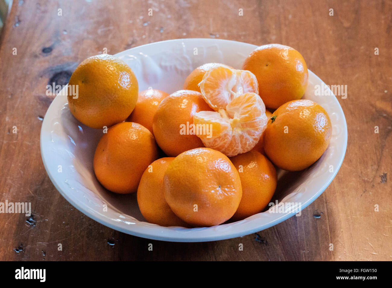 Mandarin oranges, Citrus reticulata, with one peeled, in a white bowl. Stock Photo