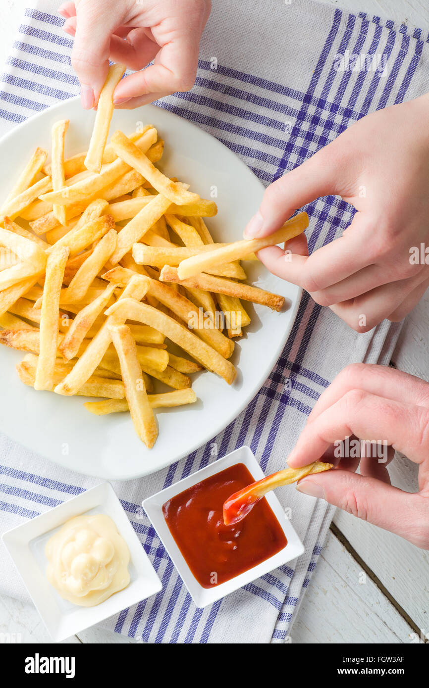 Three Hands Picking French Fries and Dipping in Ketchup and Mayonnaise