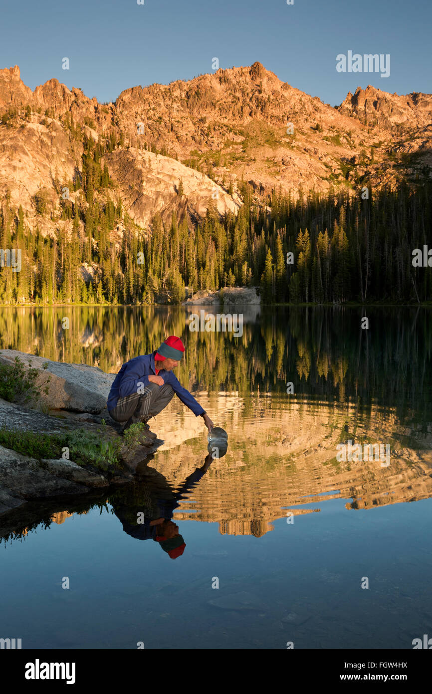 ID00339-00...IDAHO - Backpacker dipping a pan into Alpine Lake in the early morning in the Sawtooth Wilderness Area. Stock Photo