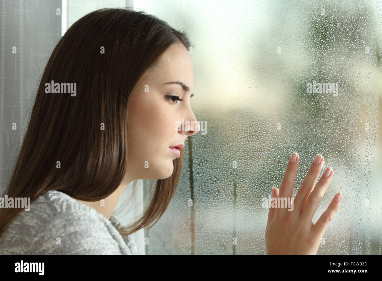 Sad woman looking the rain falling through a window at home or hotel Stock  Photo - Alamy