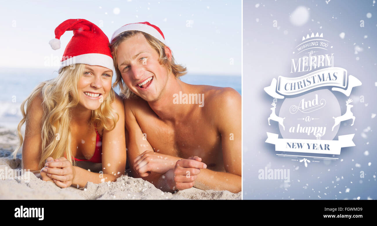 Composite image of couple lying on beach wearing christmas hats Stock Photo