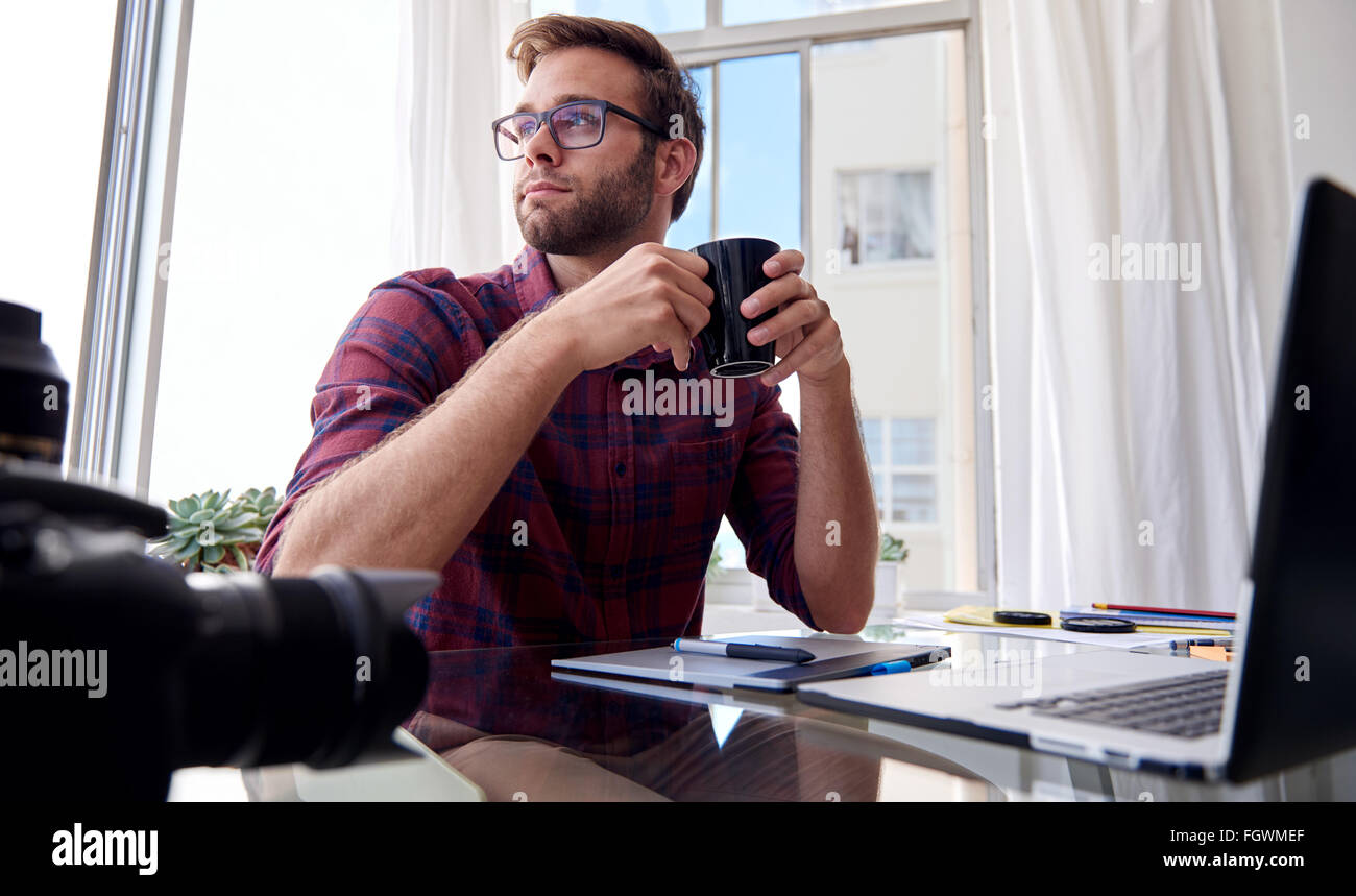 Young photographer holding coffee at his home studio Stock Photo