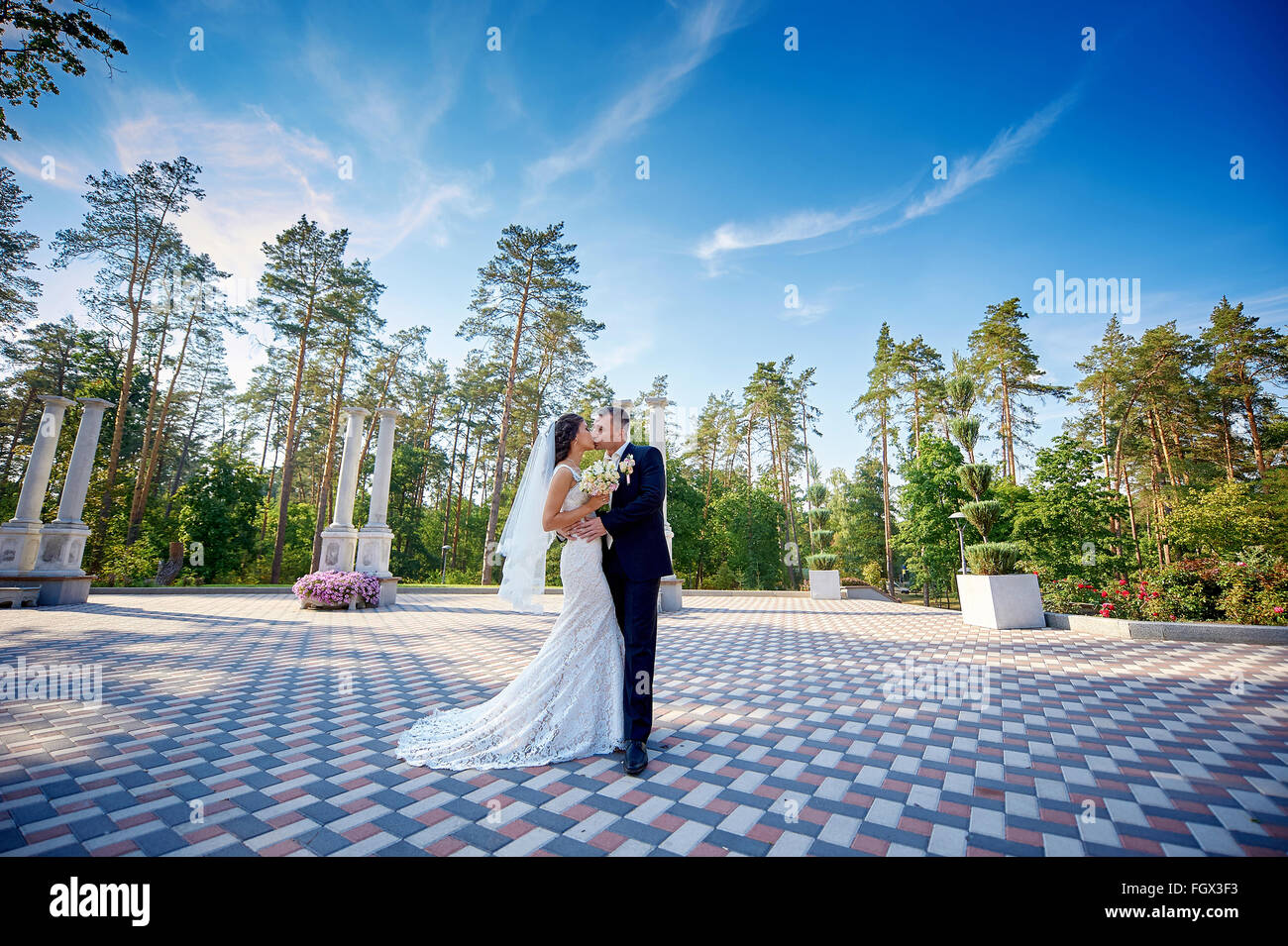 elegant stylish groom with his happy gorgeous bride kisses in the park Stock Photo