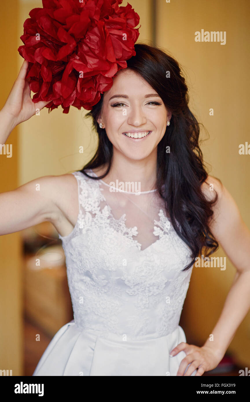 smiling bride holding a red flower on her head Stock Photo
