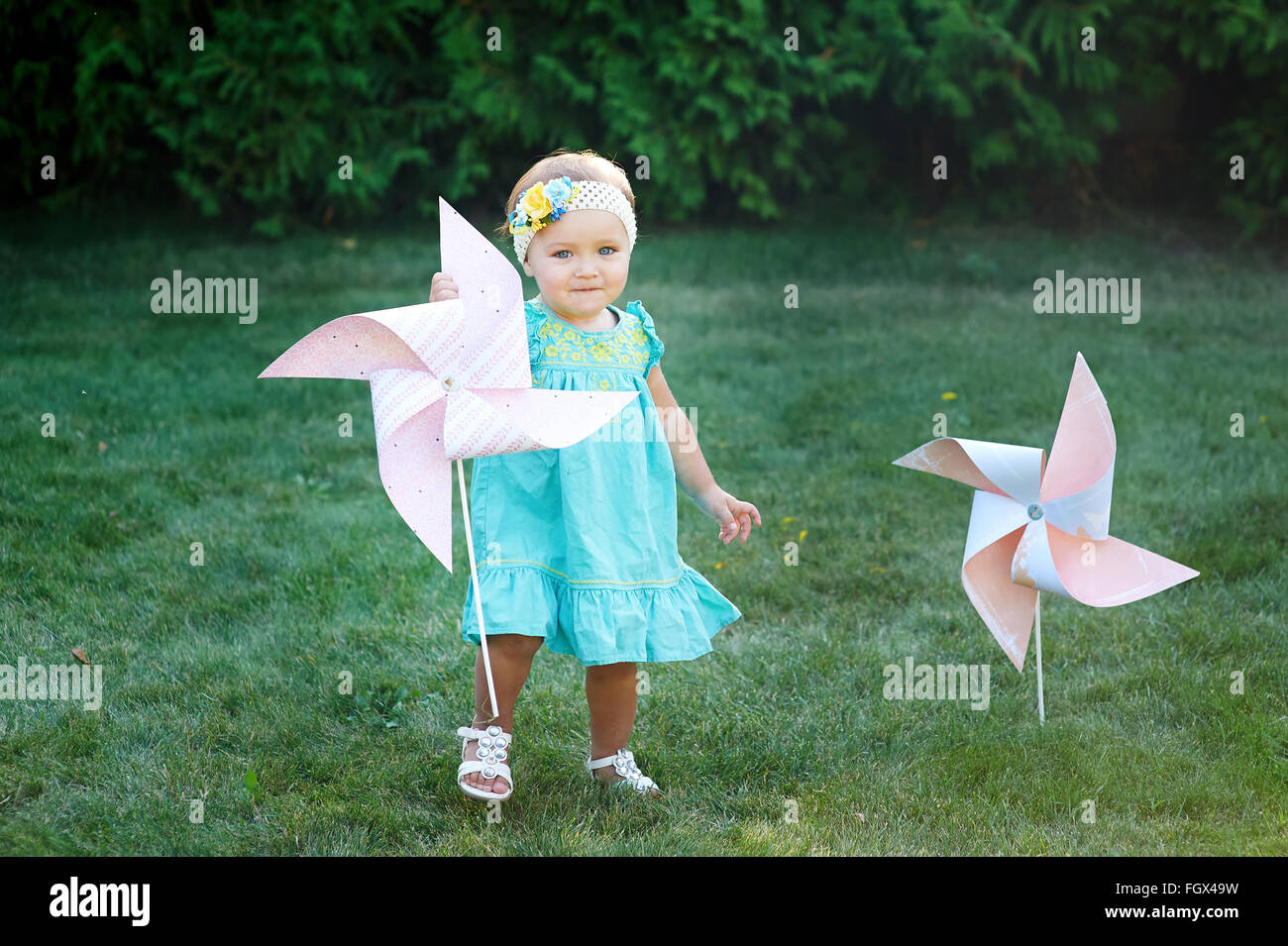 happy smiling little girl standing on meadow and holding toy white pinwheel windmill Stock Photo