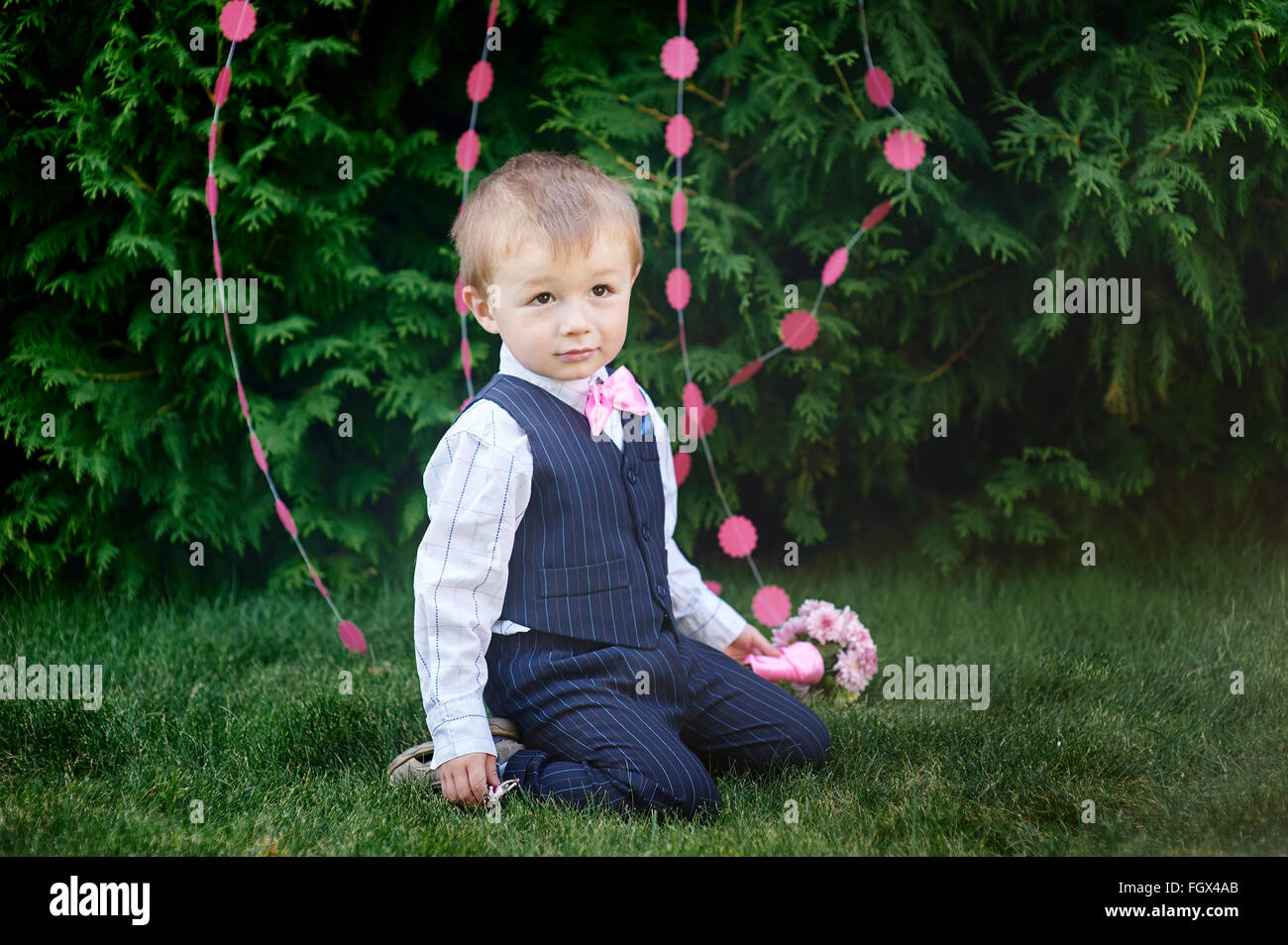little boy in a suit with a bouquet sitting on the grass Stock Photo