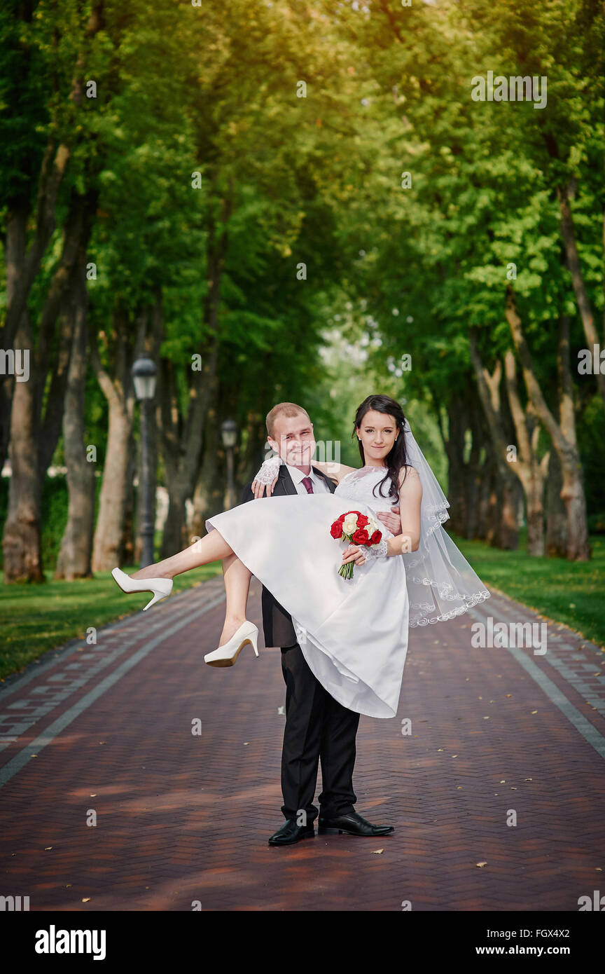 groom holds his bride in arms and smiles of happiness in summer park Stock Photo