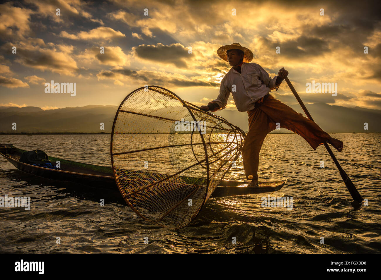 Burmese fisherman on a traditional bamboo boat catching fish  using a handmade net at sunrise Stock Photo