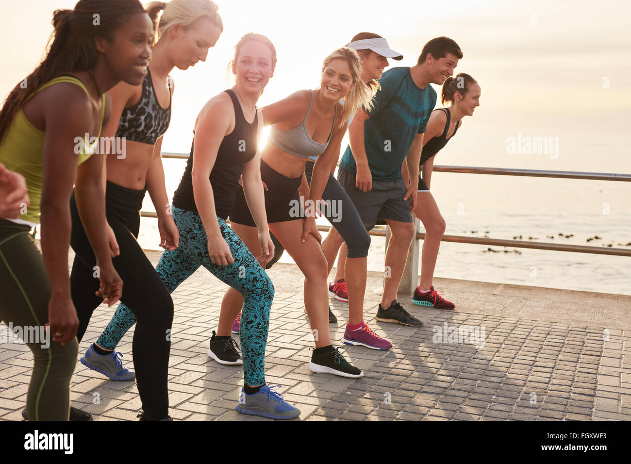 Group of young athletes in start position. Fit young people preparing for race along sea. Stock Photo
