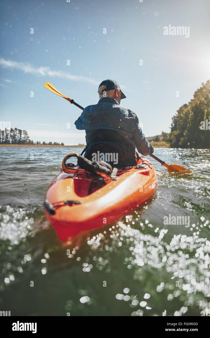 Rear view image of a mature man canoeing in a lake. Senior man paddling a kayak on summer day. Stock Photo