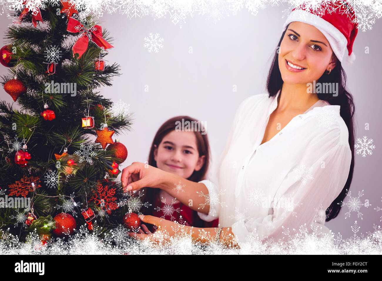 Composite image of mother and daughter hanging christmas decorations on tree Stock Photo