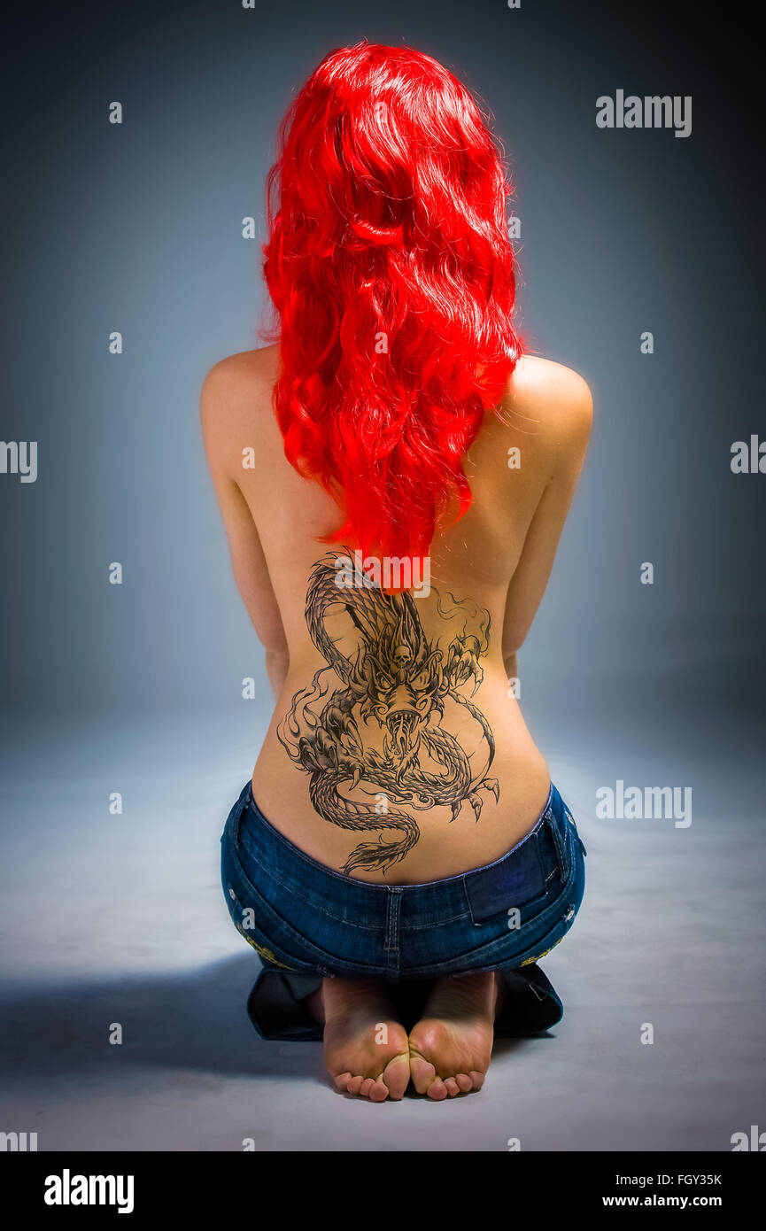 Young lady with a dragon back tattoo and red hair seated on floor Stock Photo