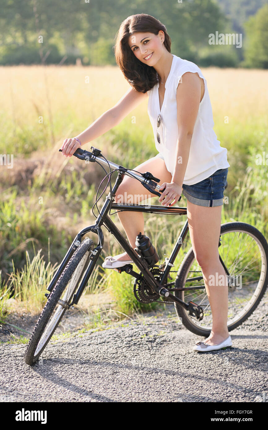 Smiling young woman with bicycle on a country road . Holidays and relax Stock Photo