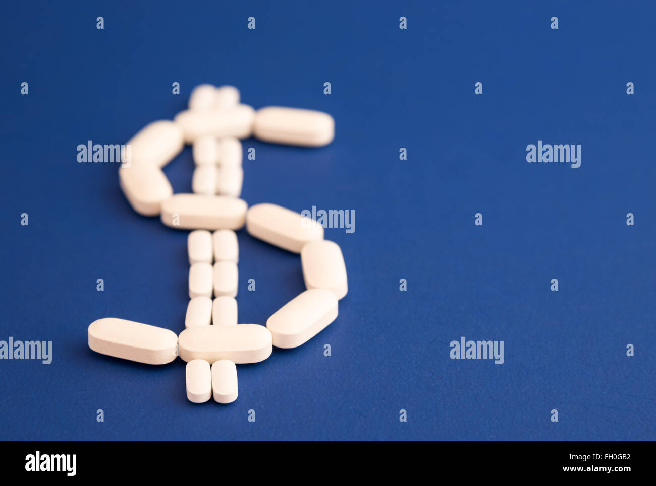 Assorted size white pills as a dollar sign, on a blue background Stock Photo