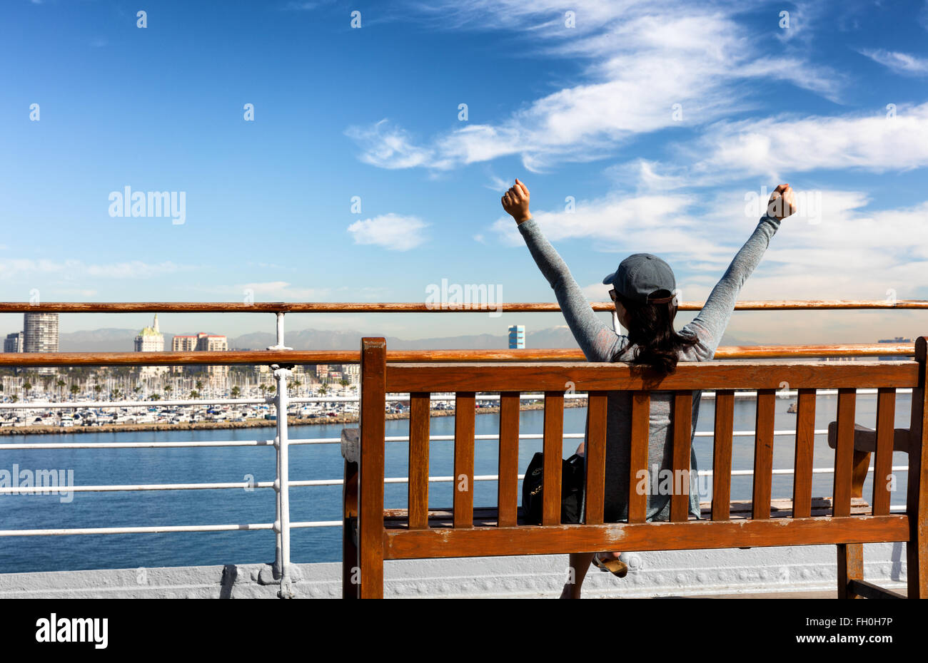 Back view of a woman stretching while sitting on bench and looking out into bay from public walkway. Stock Photo