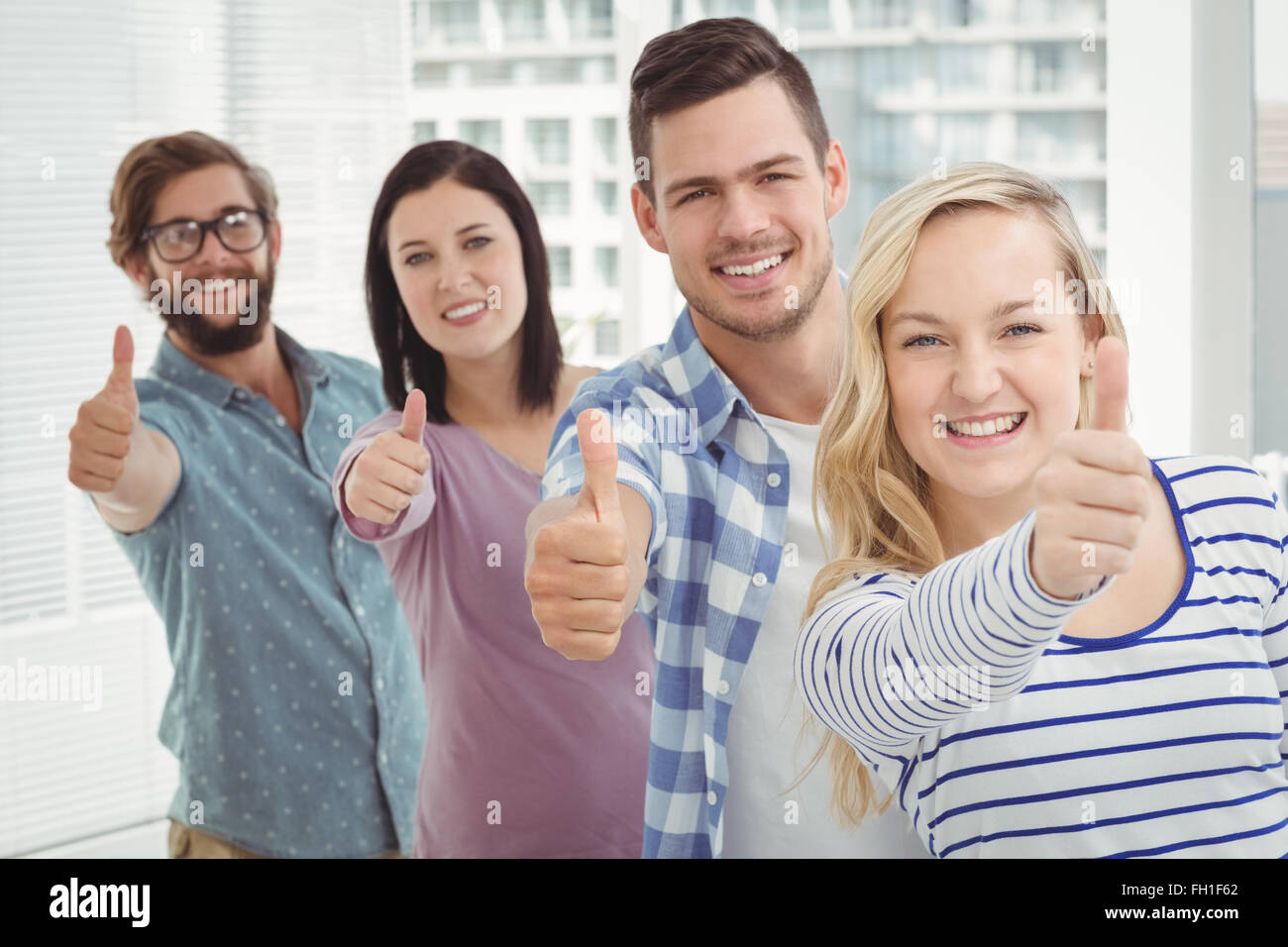 Portrait of smiling business people standing in row with thumbs up ...