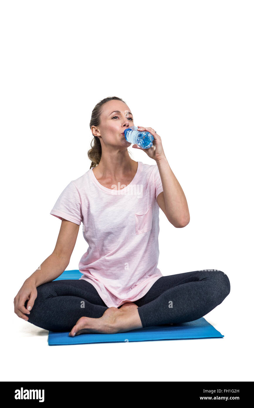 Fit woman drinking water while sitting on mat Stock Photo