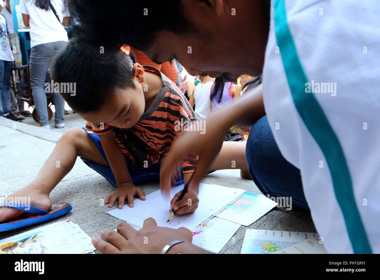 The Dynamic Teen Company (DTC) volunteers while teaching a young kid how to write his name during the Kariton Klasrum (Pushcart Classroom) conducted in Brgy. 5, Alonzo Street, Dalahikan, Cavite City. The founders of DTC find fulfillment as they slowly grow the number of youths being transformed through their programs. Transformed youth, who used to be drug users, petty thieves, scavengers, street kids, drop-outs and out-of-school youth are now DTC volunteers and have returned to mainstream education. While some of the children remain out of school they, at least, are able to access basic educa Stock Photo